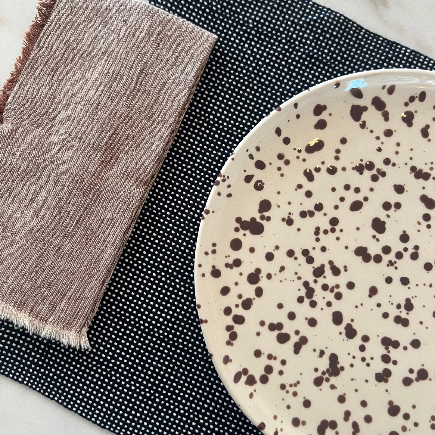 Speckled ceramic plate on a navy placemat with a brown napkin