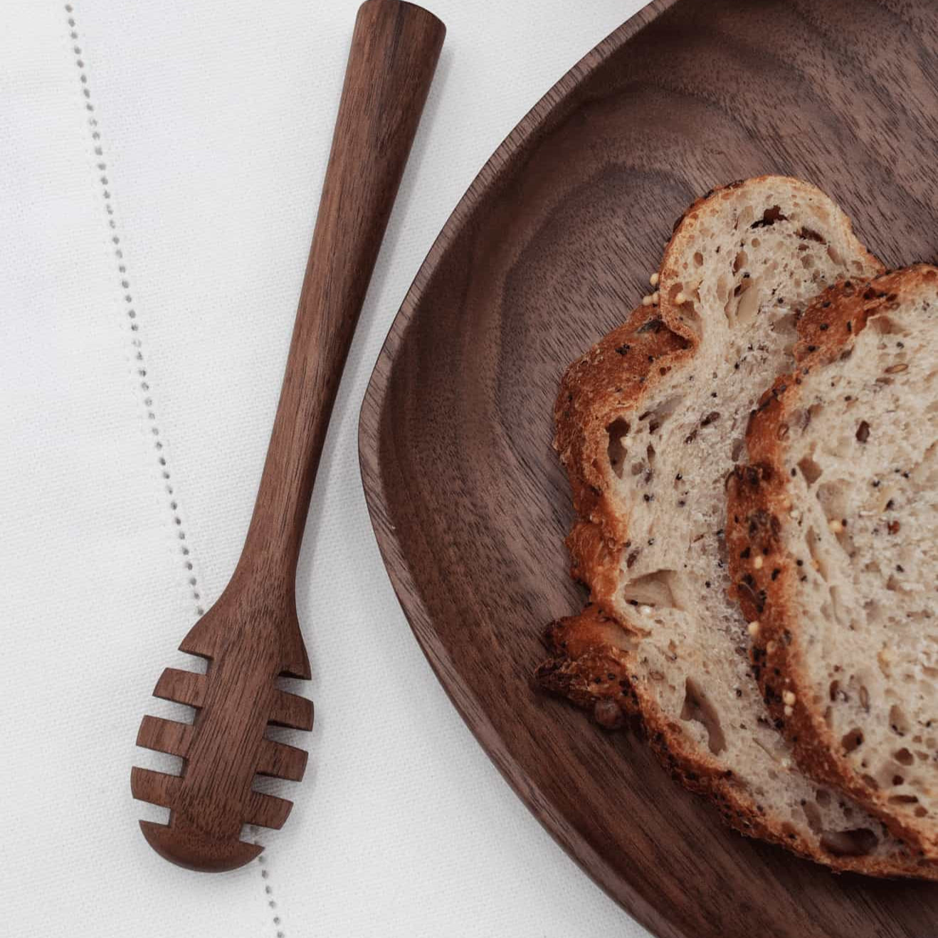 Slices of bread on a wooden plate with a wooden dipper on a white surface