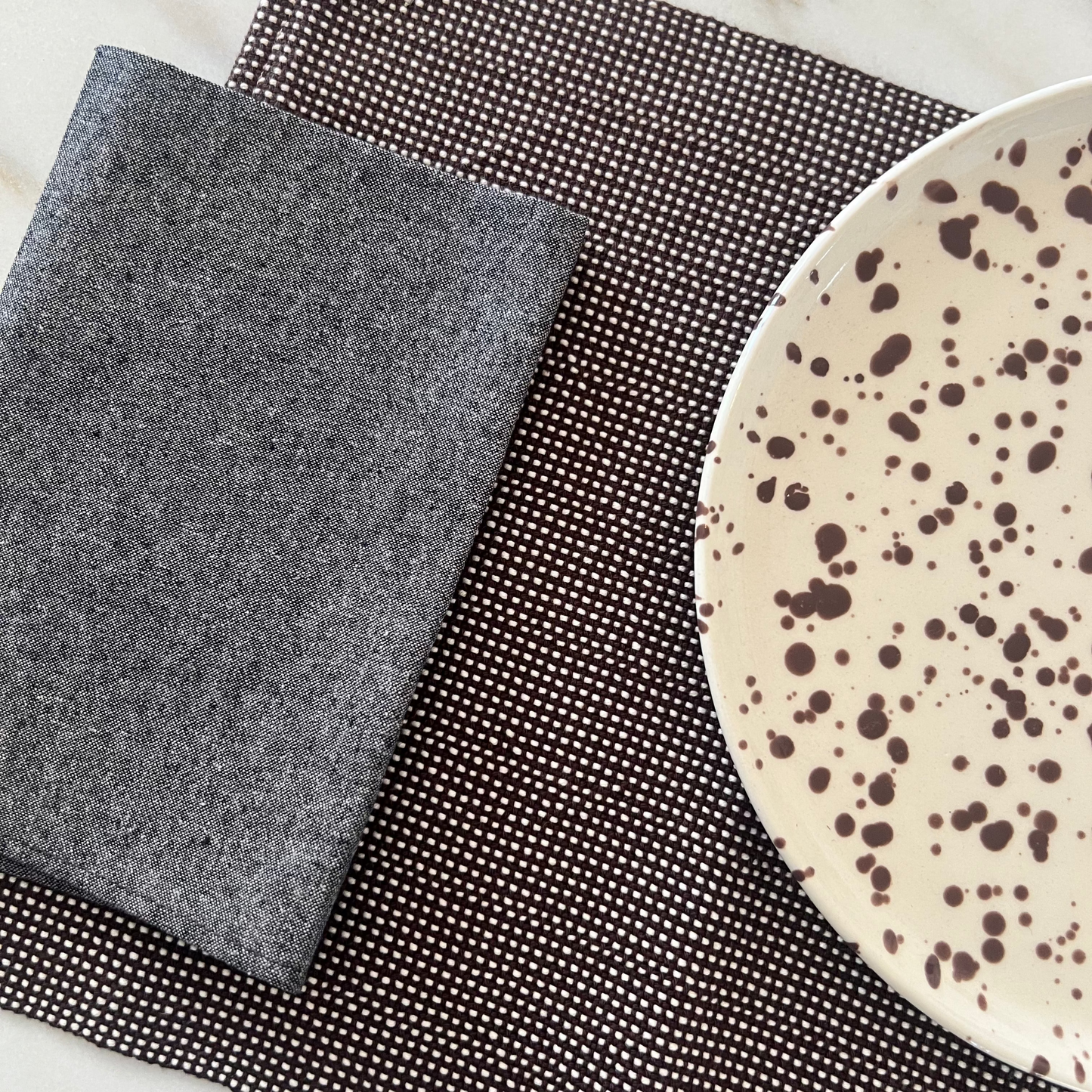 brown textured placemat with napkin and a speckled ceramic plate on a marble surface.