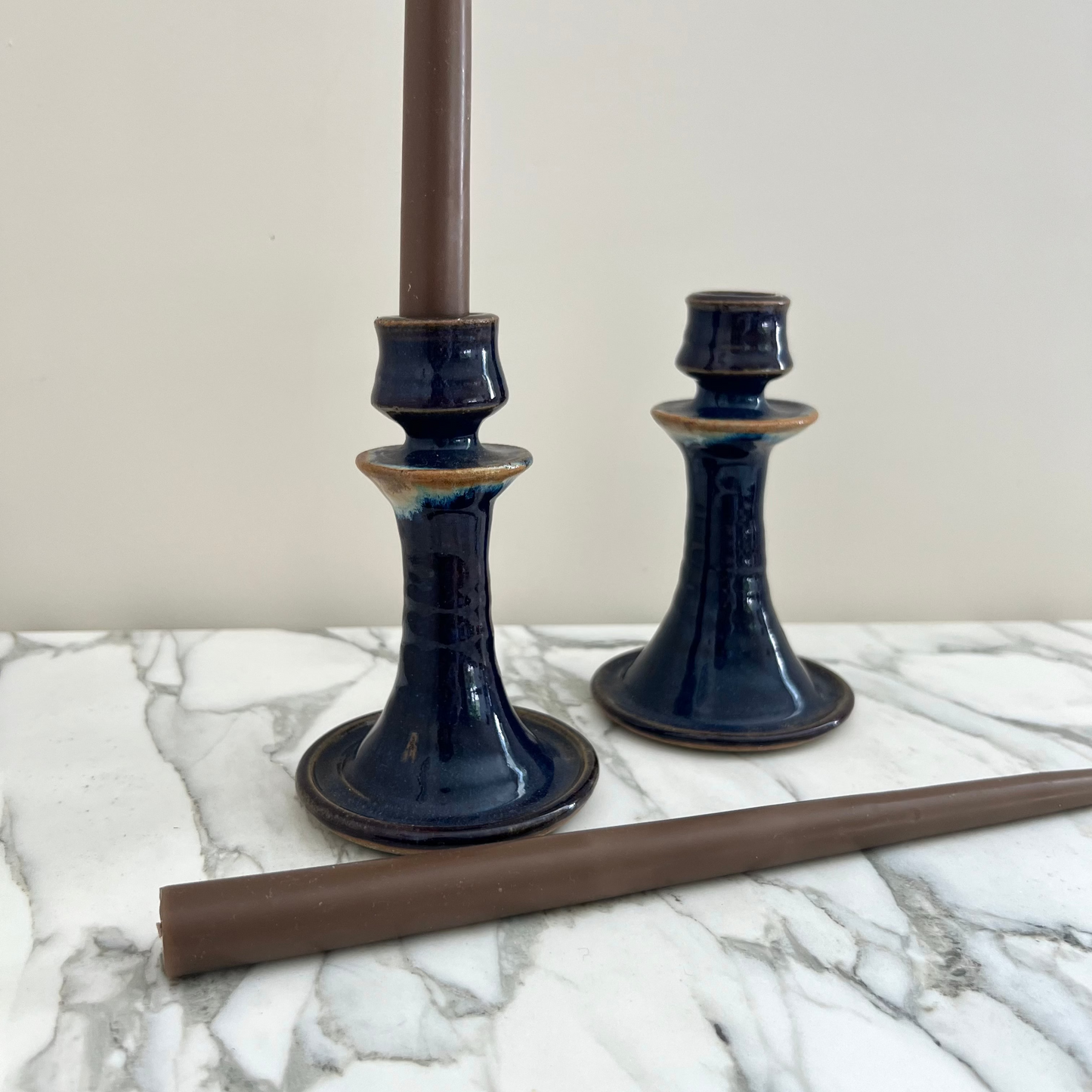 Two dark blue ceramic candle holders on a marble surface with a white background