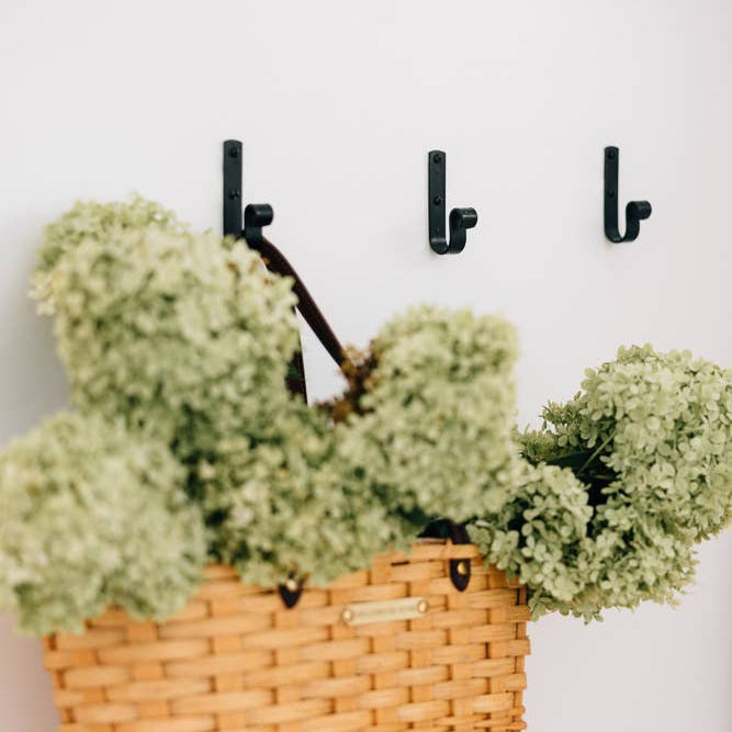 Wicker basket with green flowers hanging on a wall with black hooks.