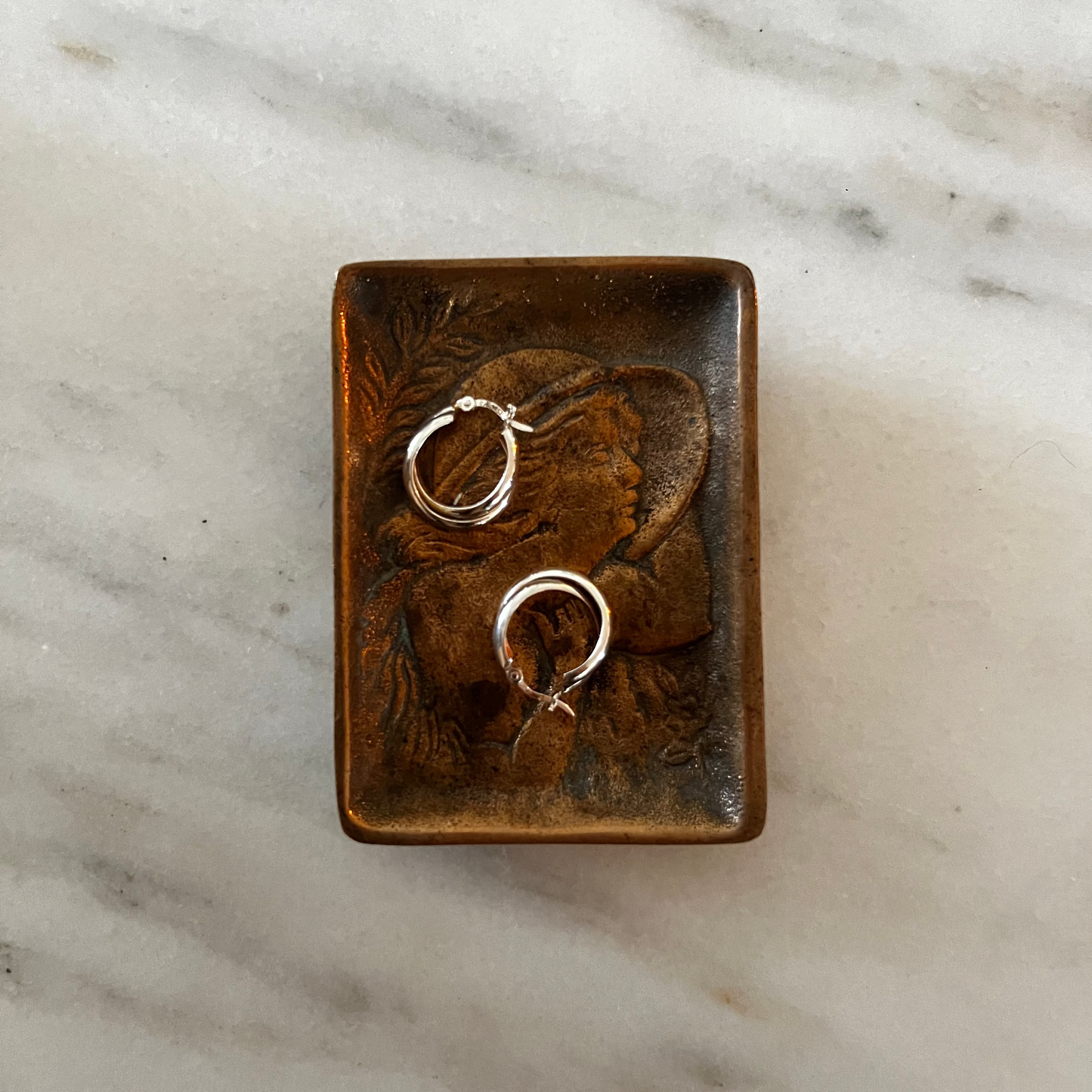 Bronze ring dish with gold rings on a marble surface