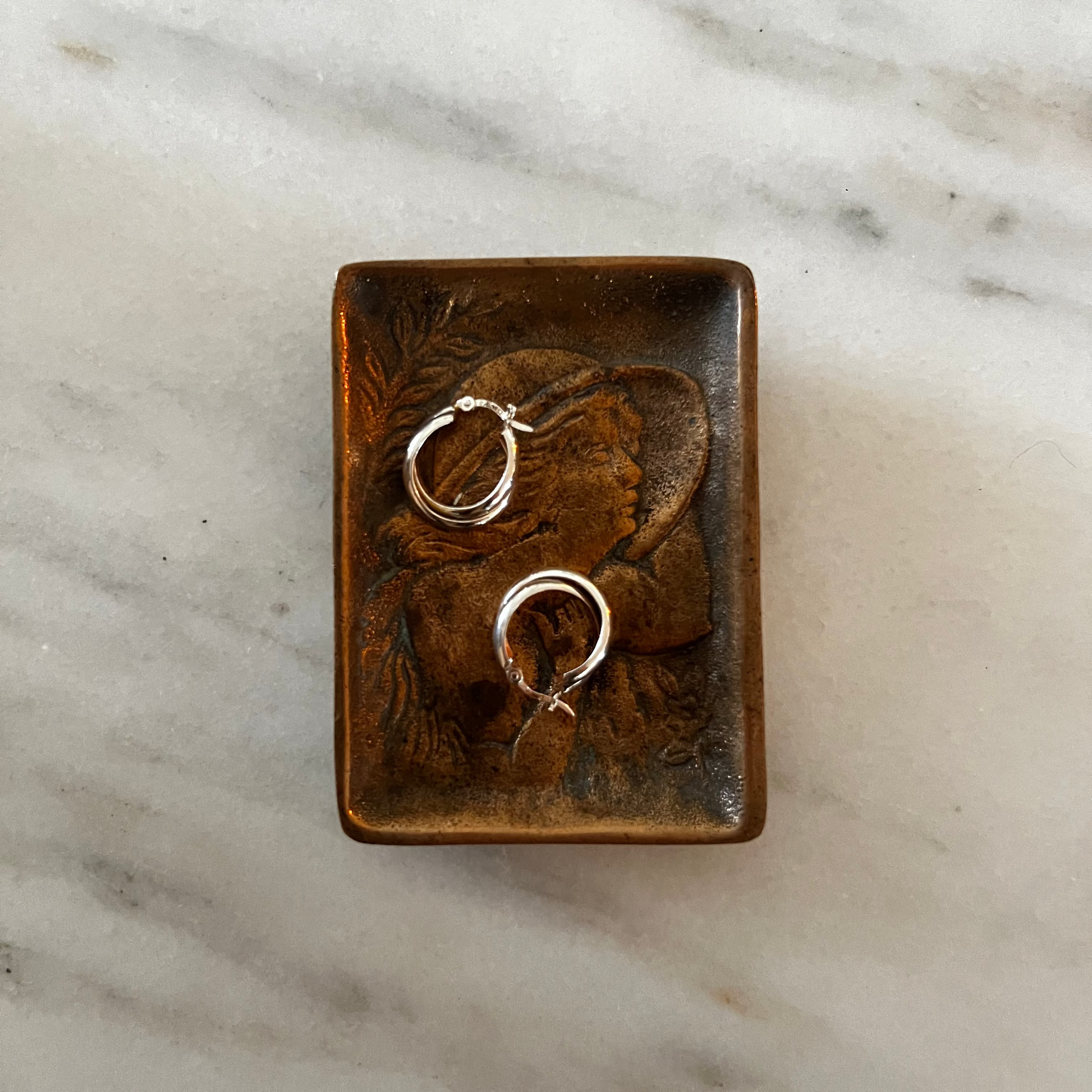 Bronze ring dish with gold rings on a marble surface