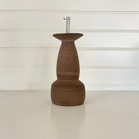 Brown ceramic bottle with a metallic cap on a white surface and light wood panel background