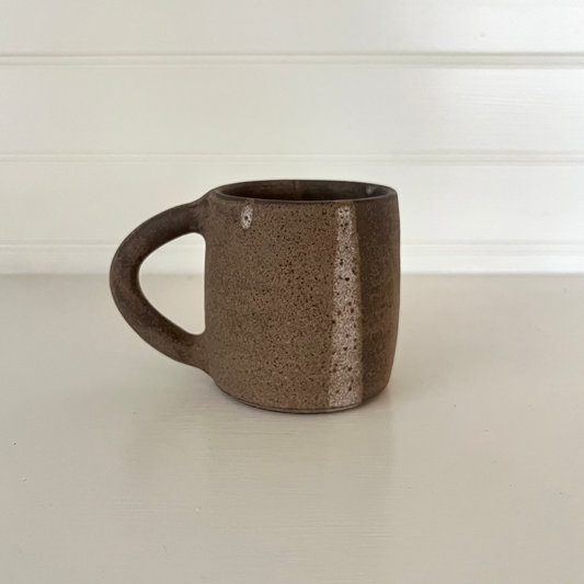 Brown ceramic mug on a white surface with a white background
