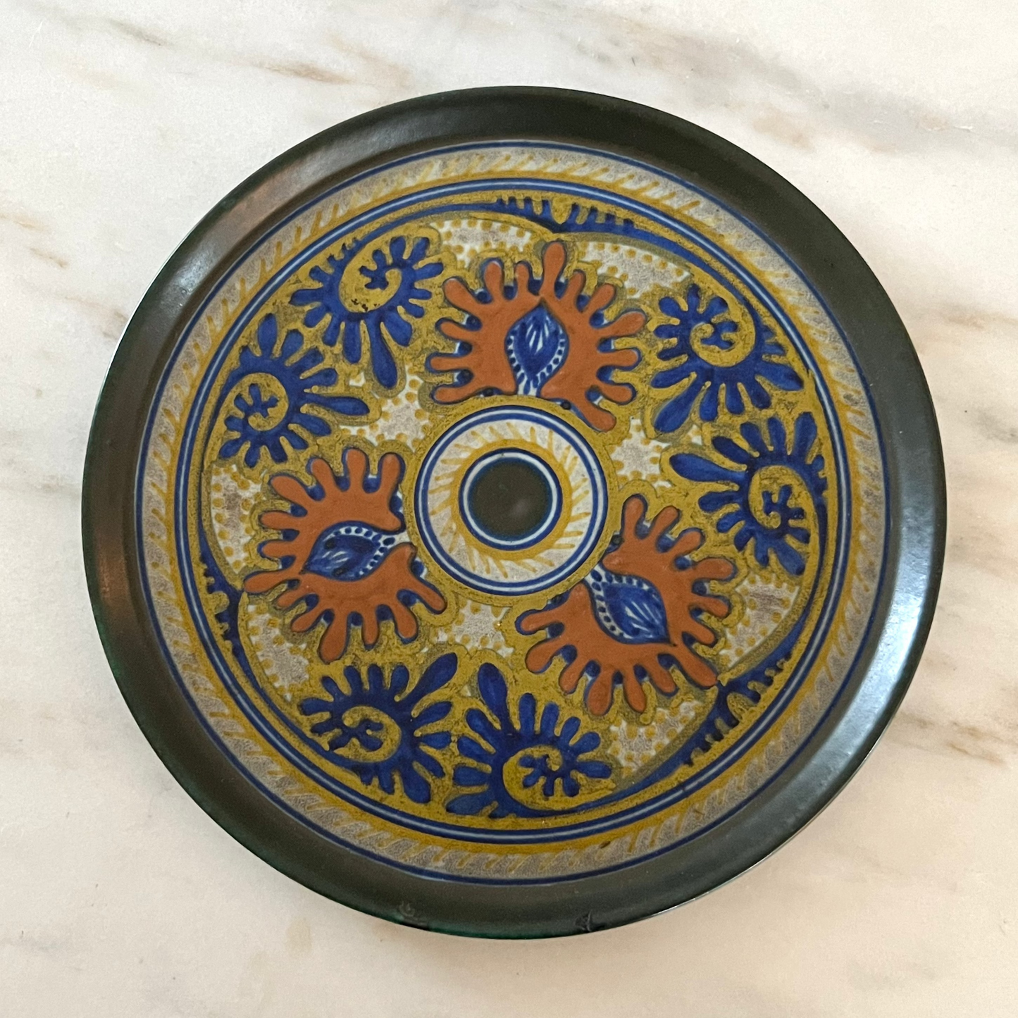 Decorative ceramic plate with blue and orange patterns on a marble surface
