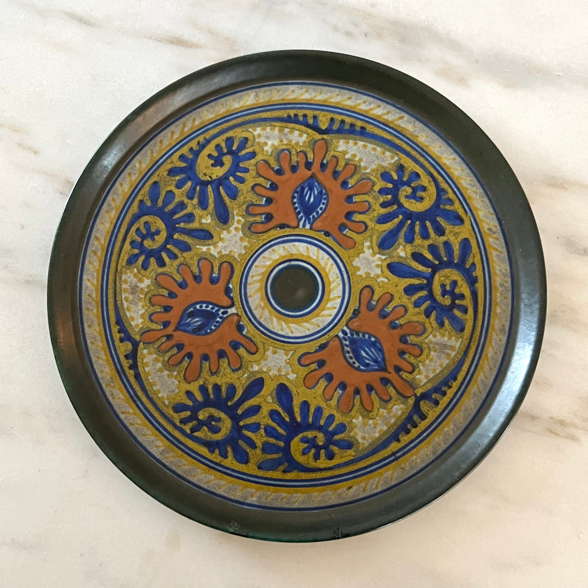 Decorative ceramic plate with blue and orange patterns on a marble surface