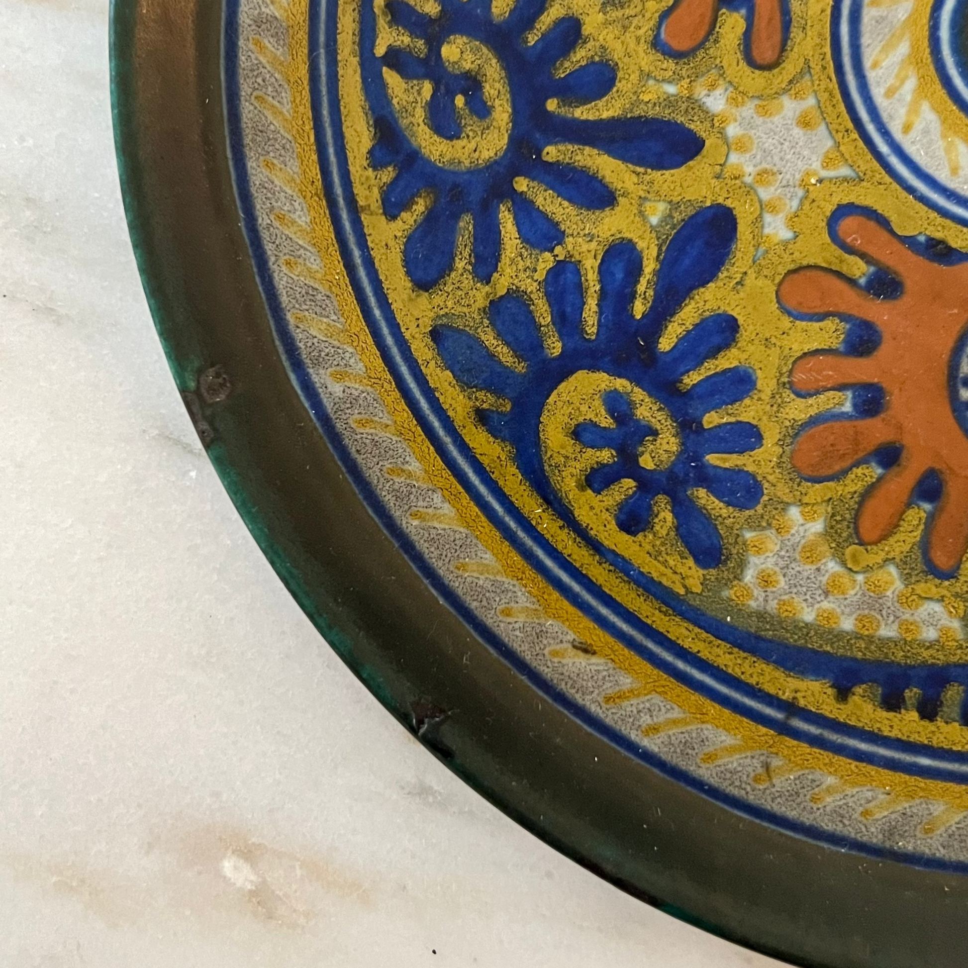 Decorative plate with blue and orange floral patterns on a marble surface