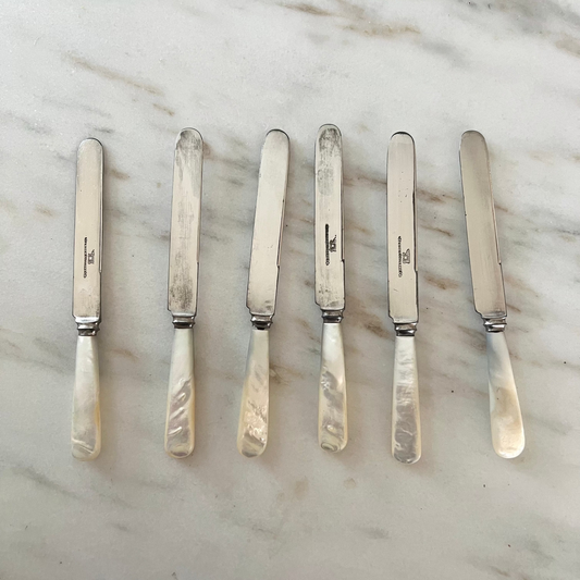 Set of silver butter knives with mother-of-pearl handles on a marble surface