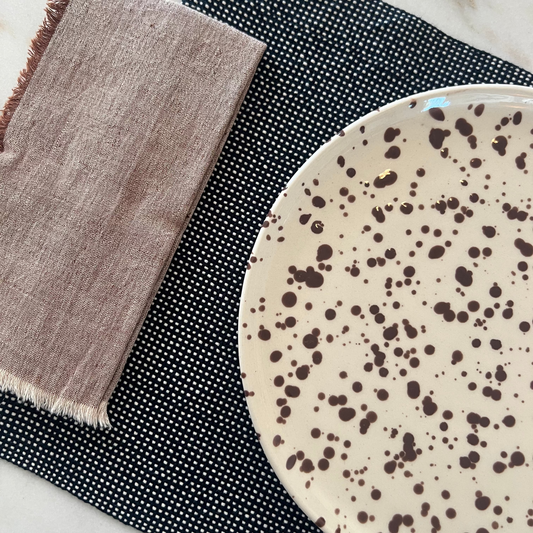Speckled ceramic plate on a navy placemat with a brown napkin