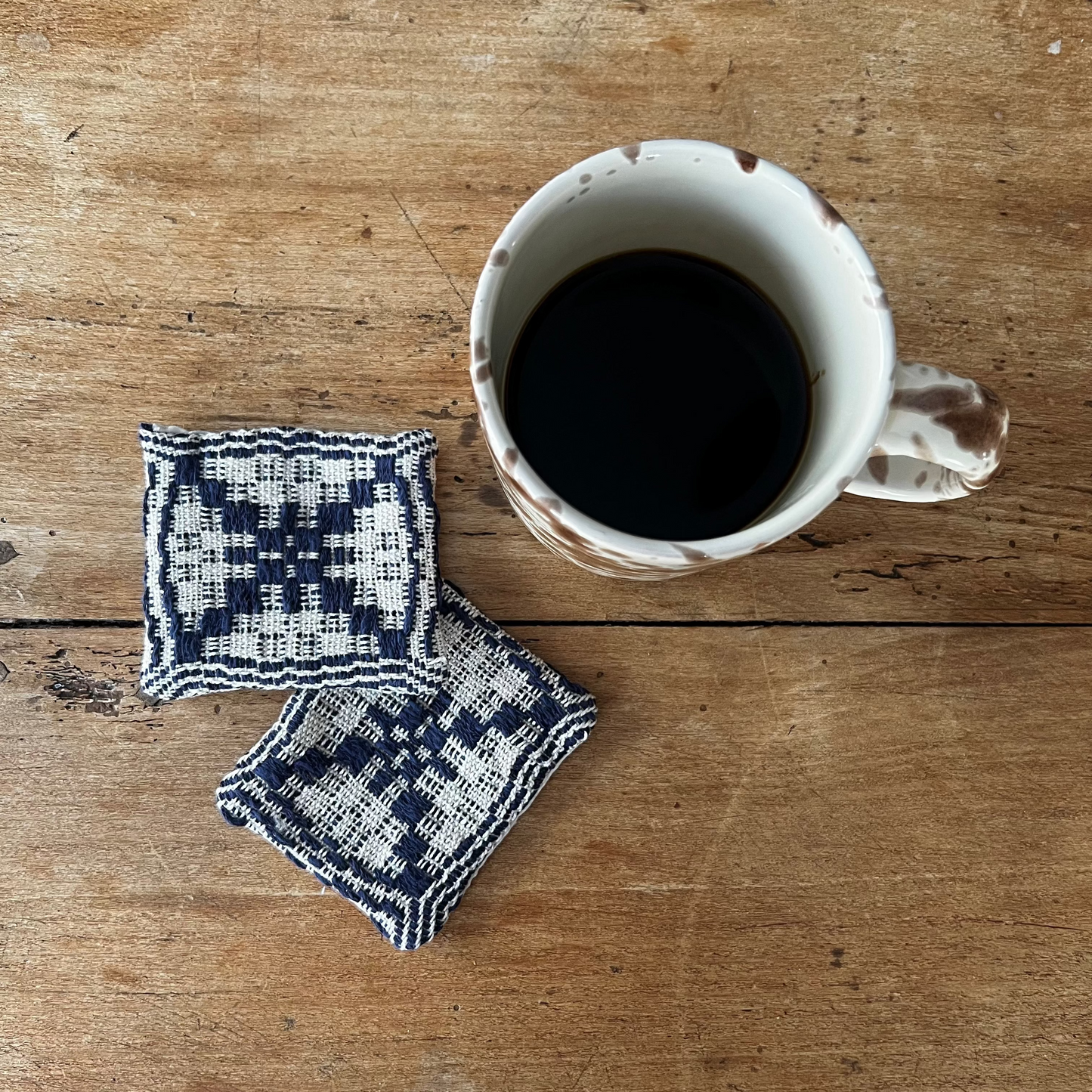 Cup of coffee with two patterned coasters on a wooden surface