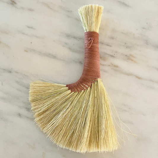 Small broom with a brown handle on a marble surface
