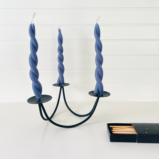 Three twisted blue candles in a black metal candle holder on a white background.