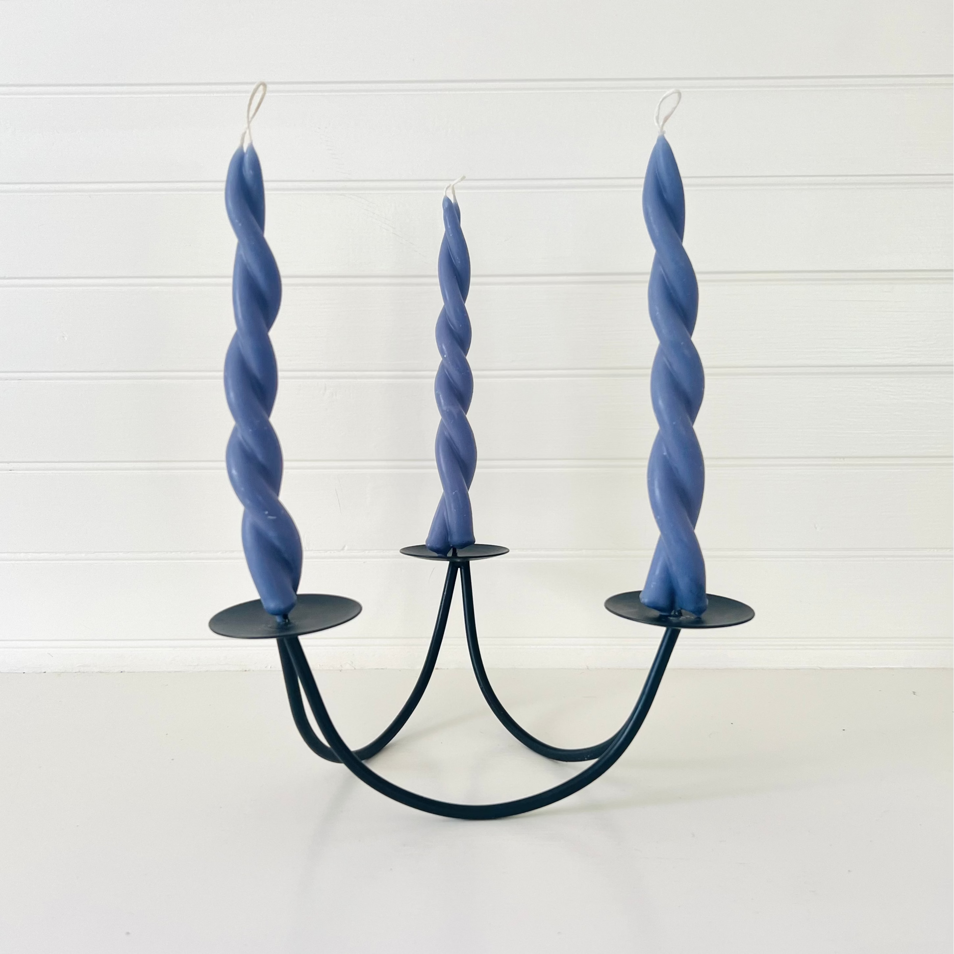 Twisted blue candles on a black candle holder against a white background