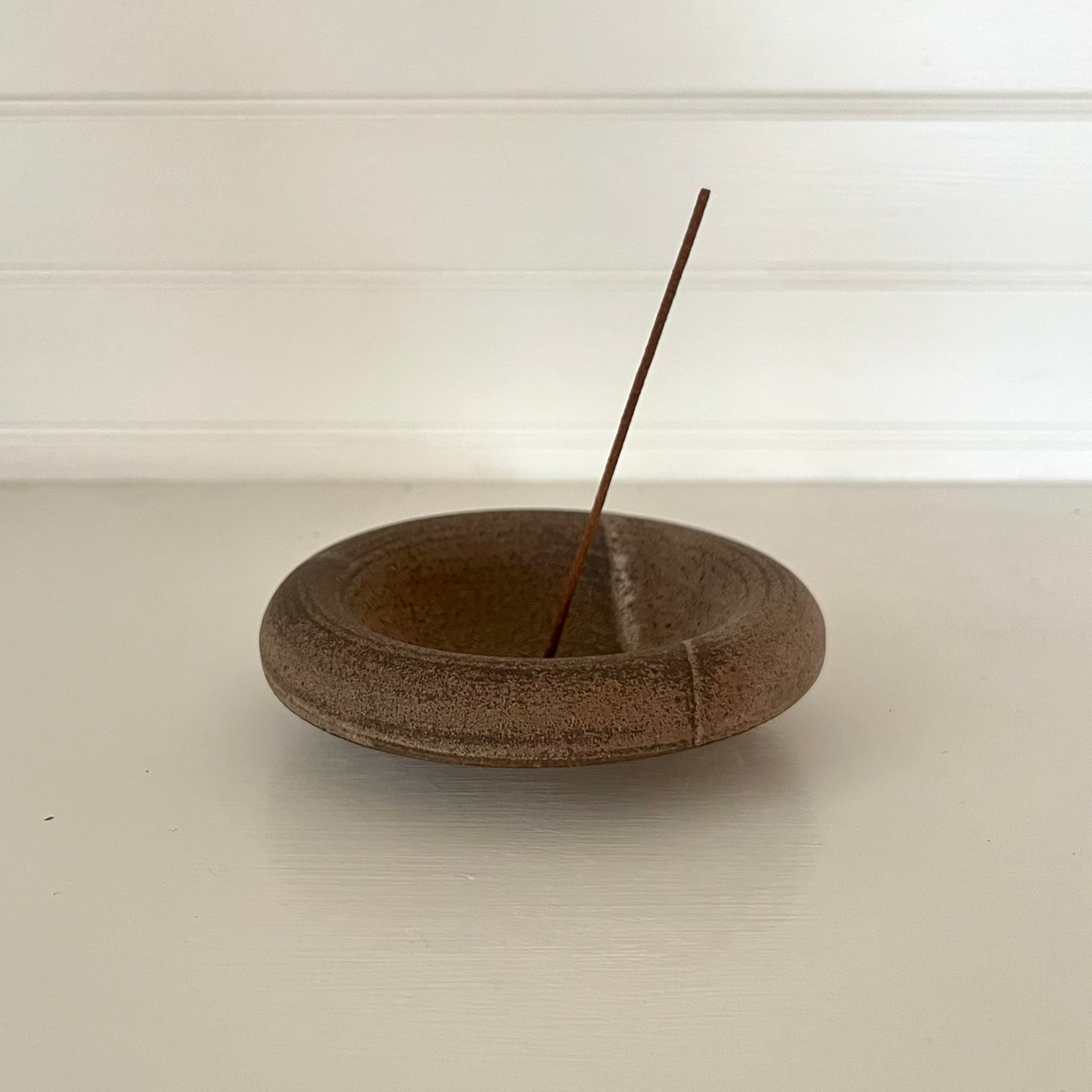 Wooden incense holder with a single incense stick on a white surface.