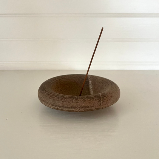 Wooden incense holder with a single incense stick on a white surface.