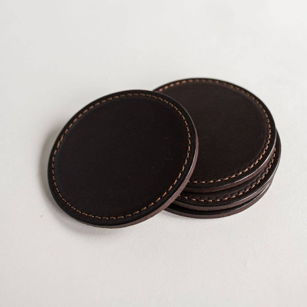 Set of dark brown leather coasters on a light gray background