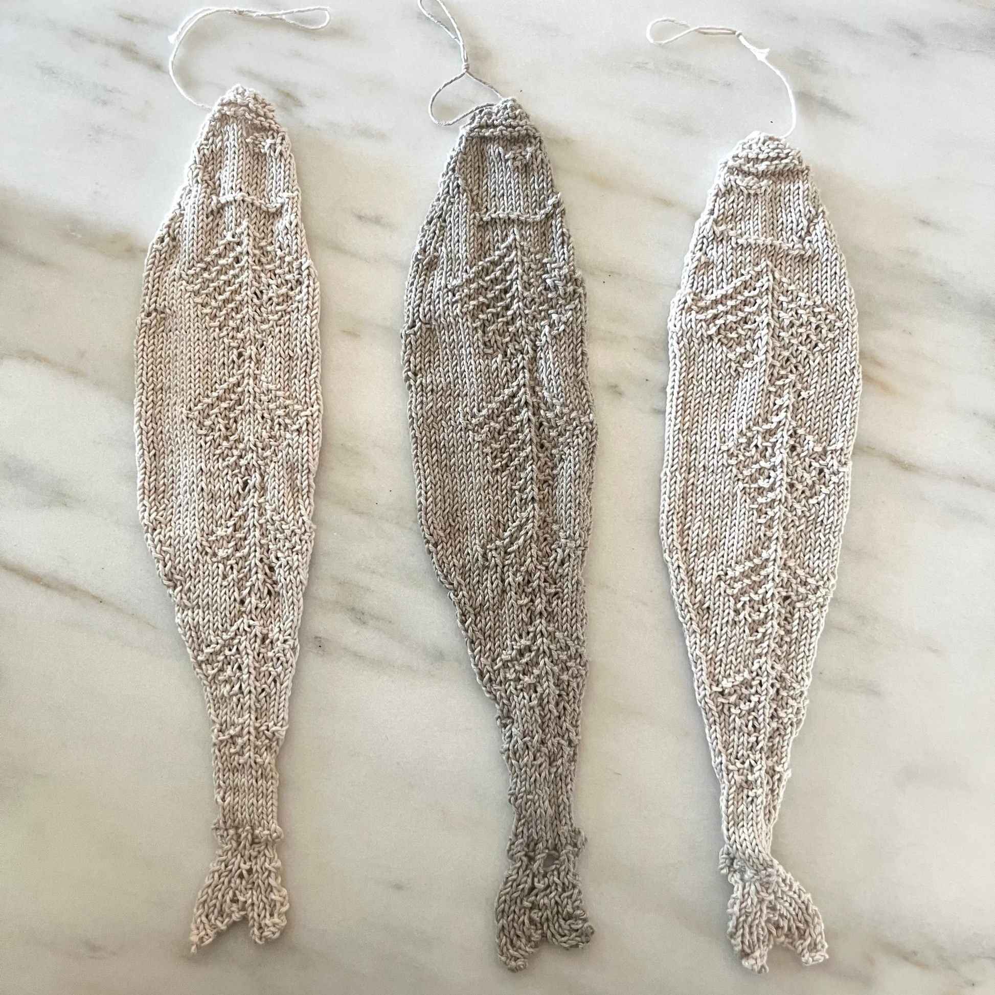 Three knitted fish-shaped objects on a marble surface with a textured rug in the background.