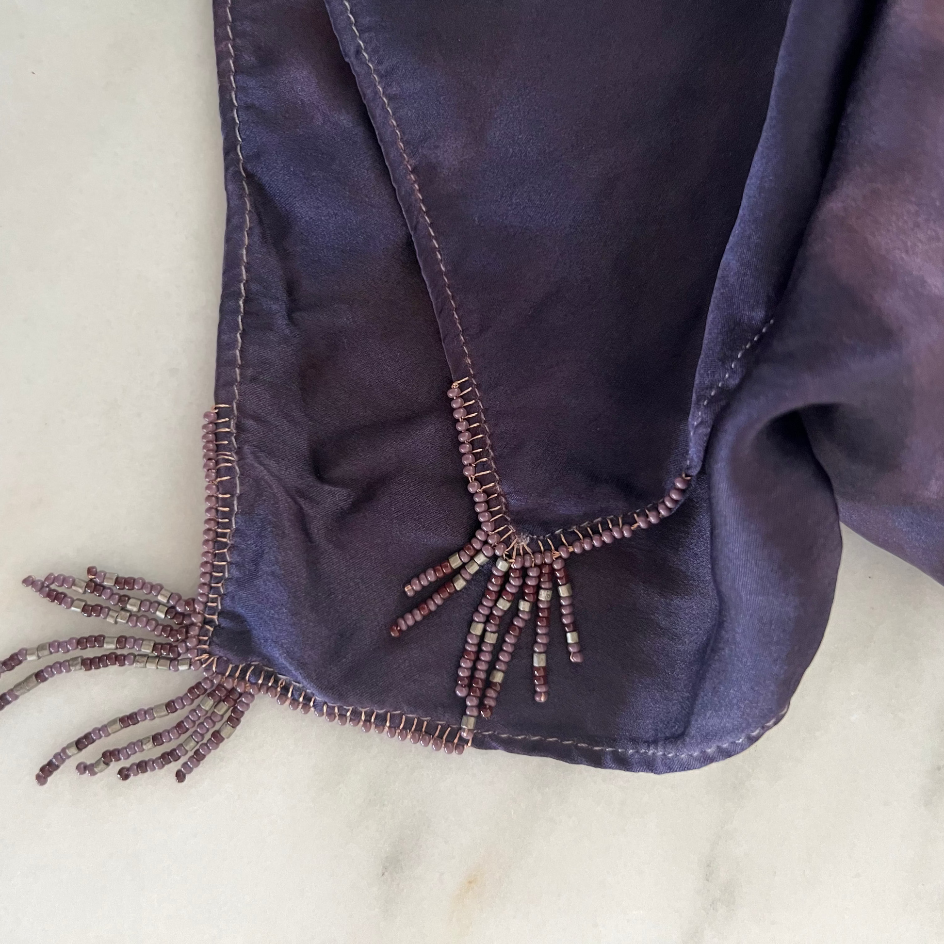 Close-up of a dark purple fabric with beaded detailing on a light marble background