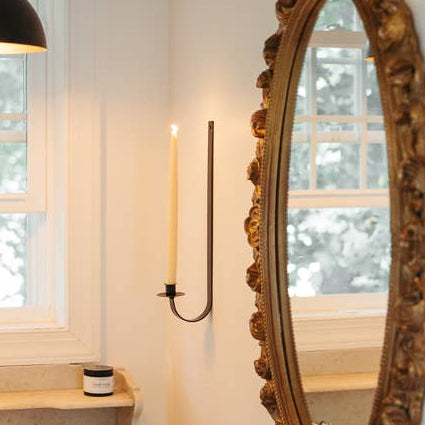 Decorative oval mirror on a wall with a candle and window in the background
