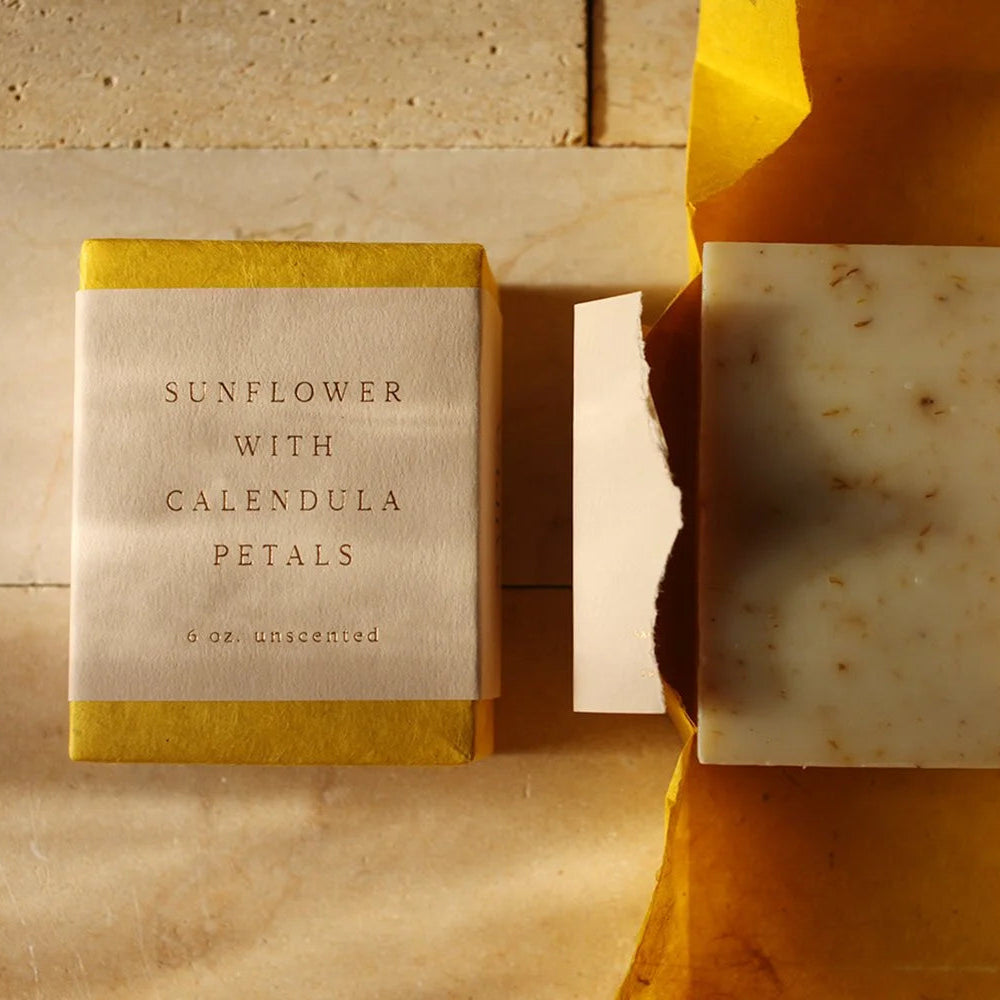 Bar of soap with packaging labeled 'Sunflower with Calendula Petals' on a stone surface.